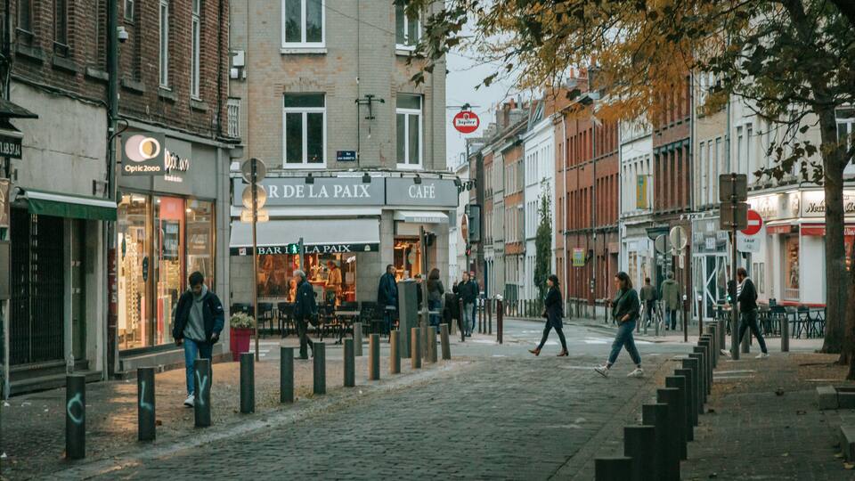 Eine Kopfsteinpflasterstraße gesäumt von Cafés und Geschäften, Fußgänger unterwegs, und ein Verbotsschild.