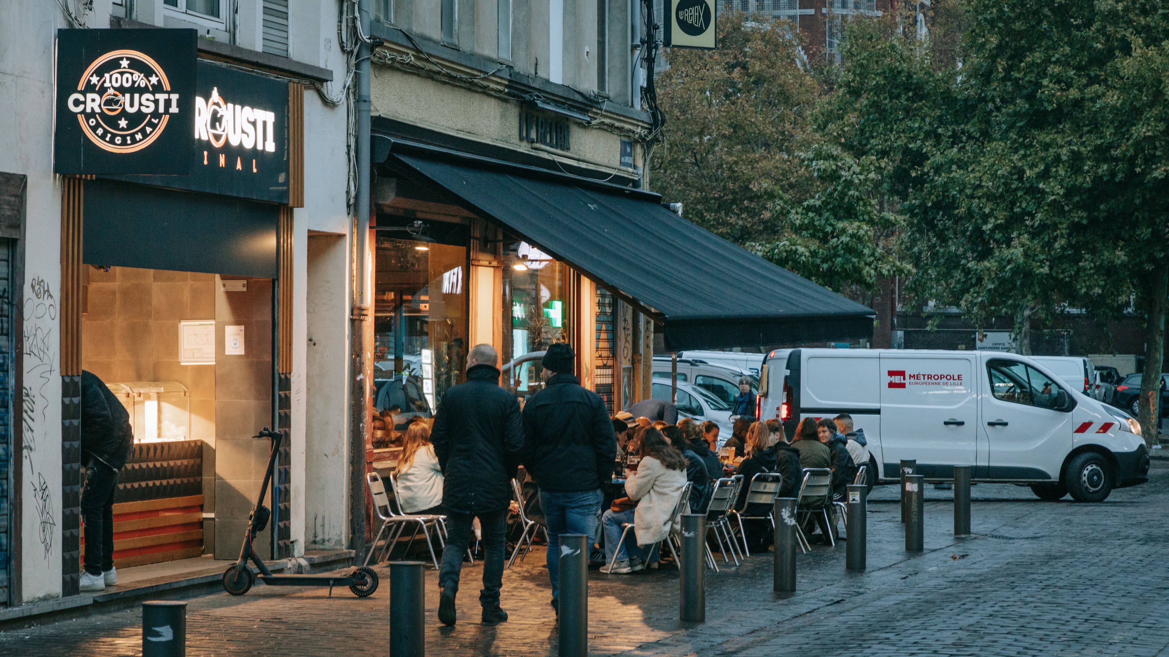 Un restaurante Crosti con terraza, una furgoneta blanca y personas comiendo.