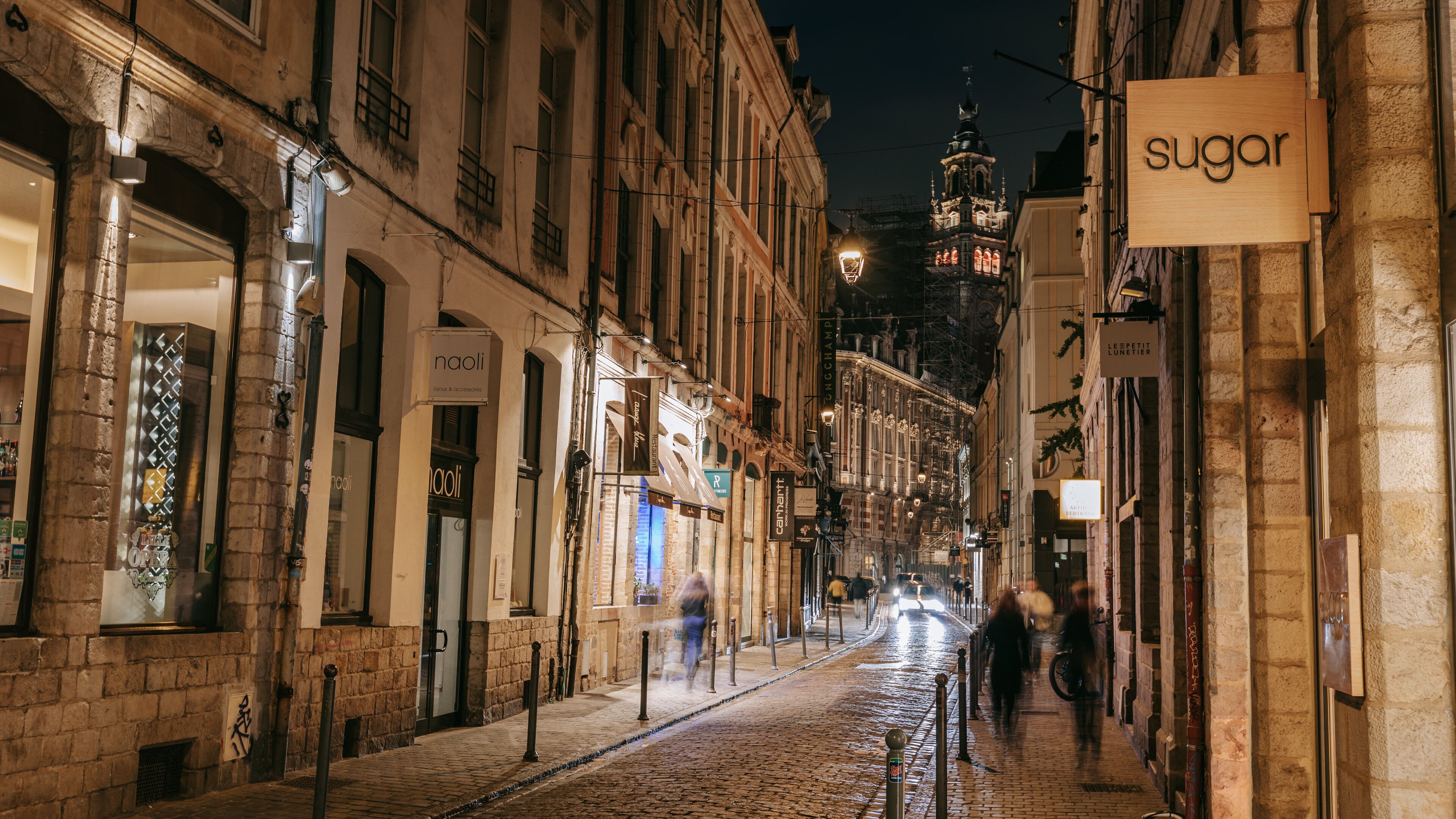 Una calle adoquinada flanqueada por edificios históricos, iluminada por farolas y letreros de tiendas.