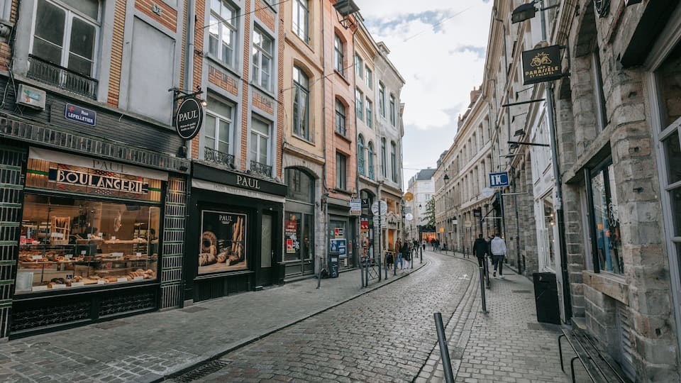 Une rue pavée bordée de bâtiments historiques, de boutiques et d’une voie ferrée pour tramway.