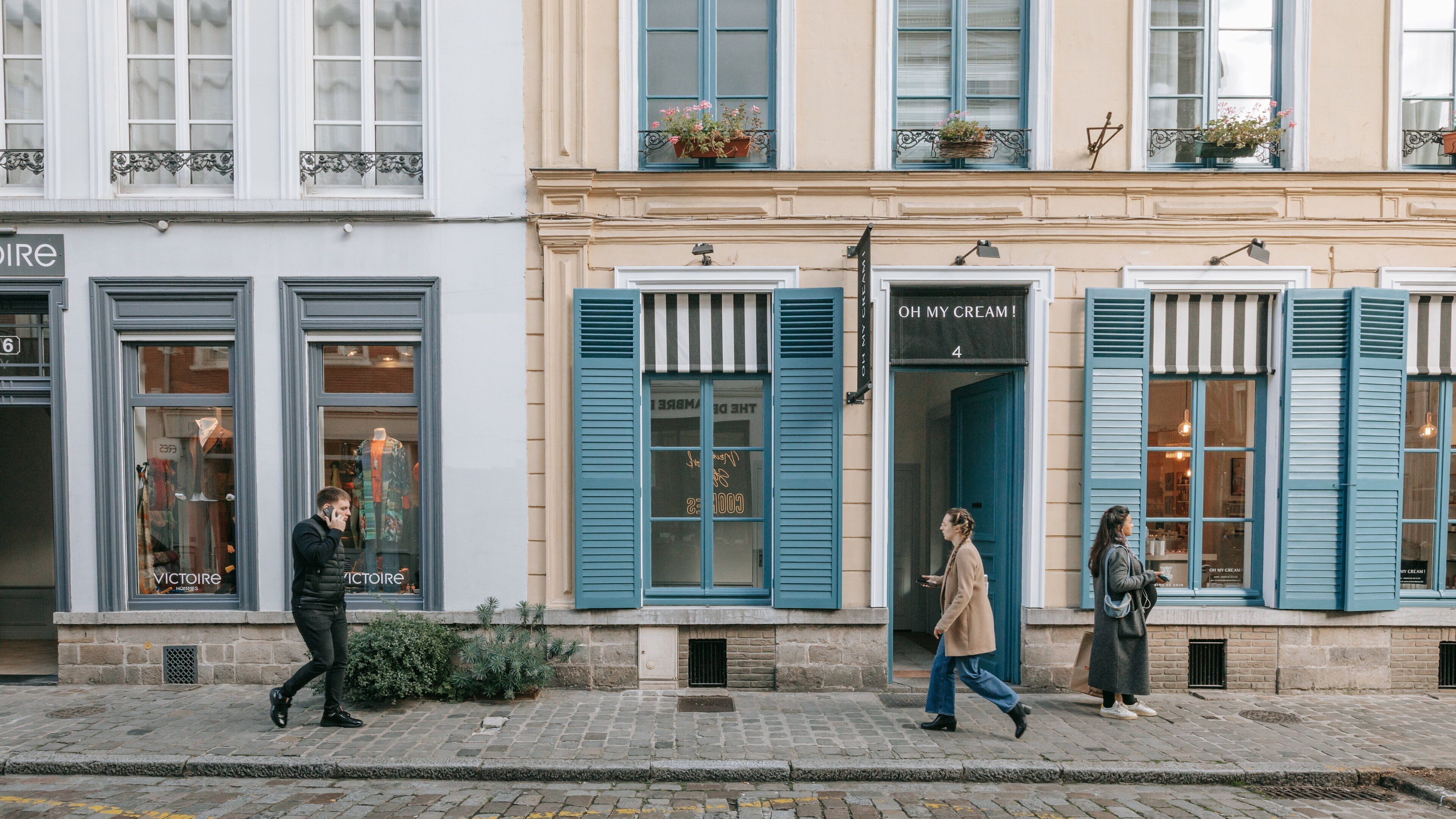 A street with a shop named "VICTOIRE" and another shop with blue shutters and a sign that says "OH MY CREAM!".