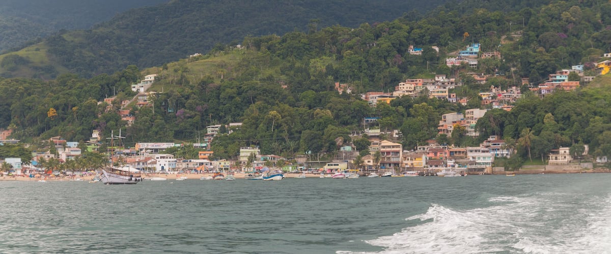 A coastal town with colorful buildings, a beach, and a mountainous backdrop.