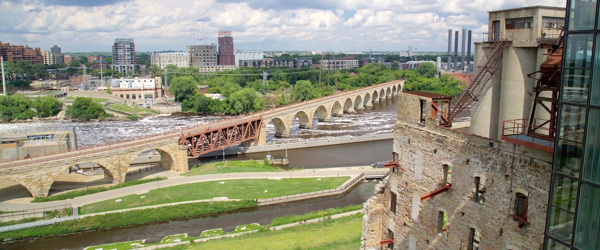 A stone bridge over a river, surrounded by greenery and urban buildings.