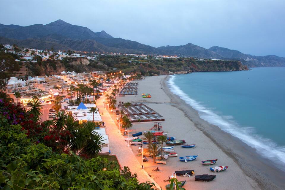A coastal town with a beach, boats, and mountains in the background.