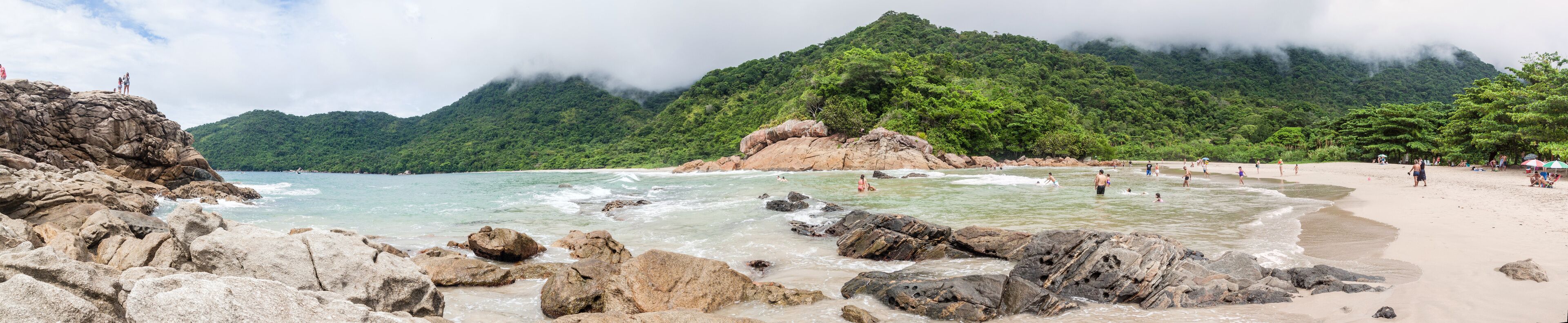 A beach with rocky shores, clear turquoise water, and lush green mountains in the background.