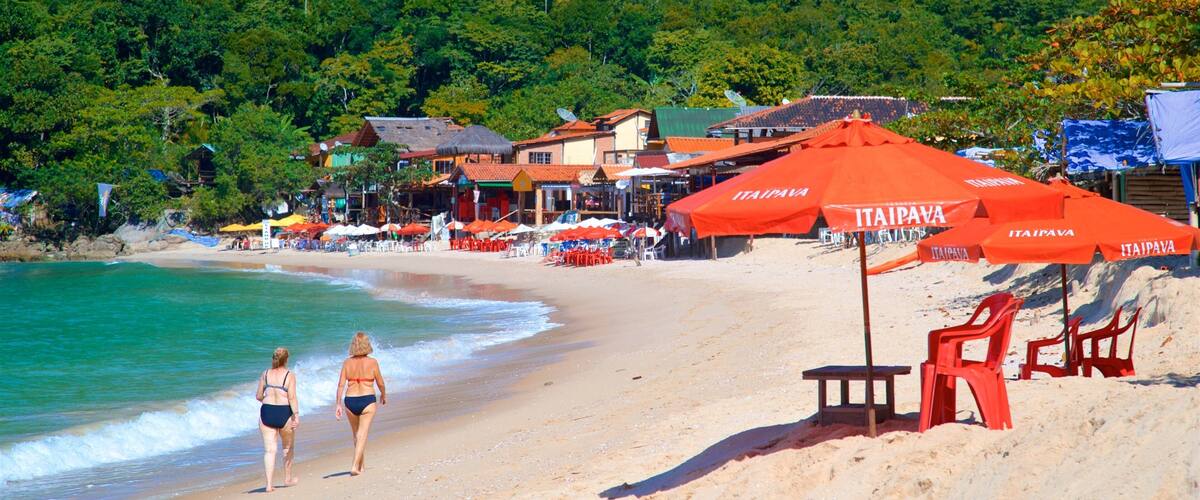 A beach with red umbrellas, a sandy shore, and a forested hill in the background.