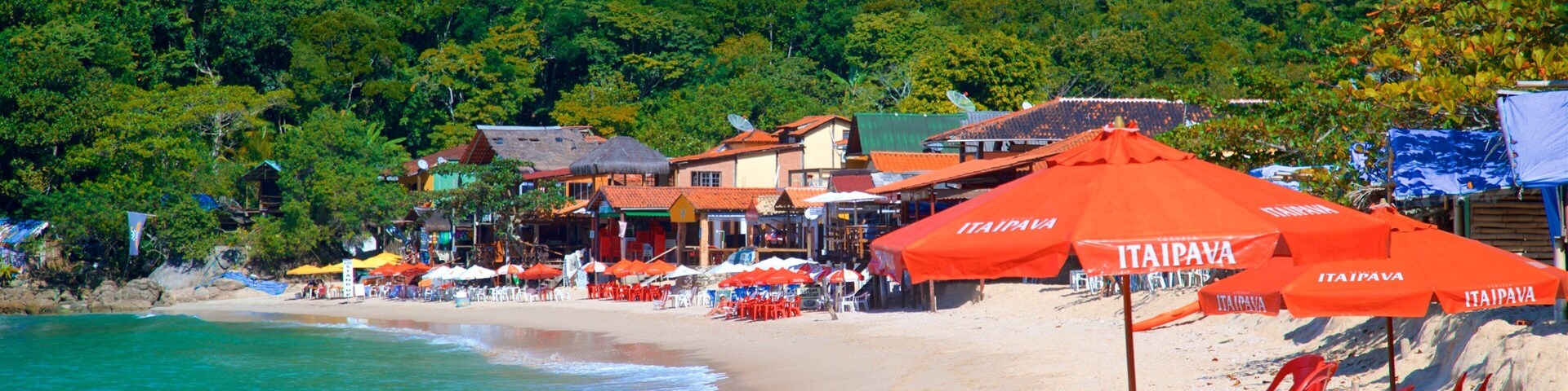 A beach with red umbrellas, a sandy shore, and a forested hill in the background.