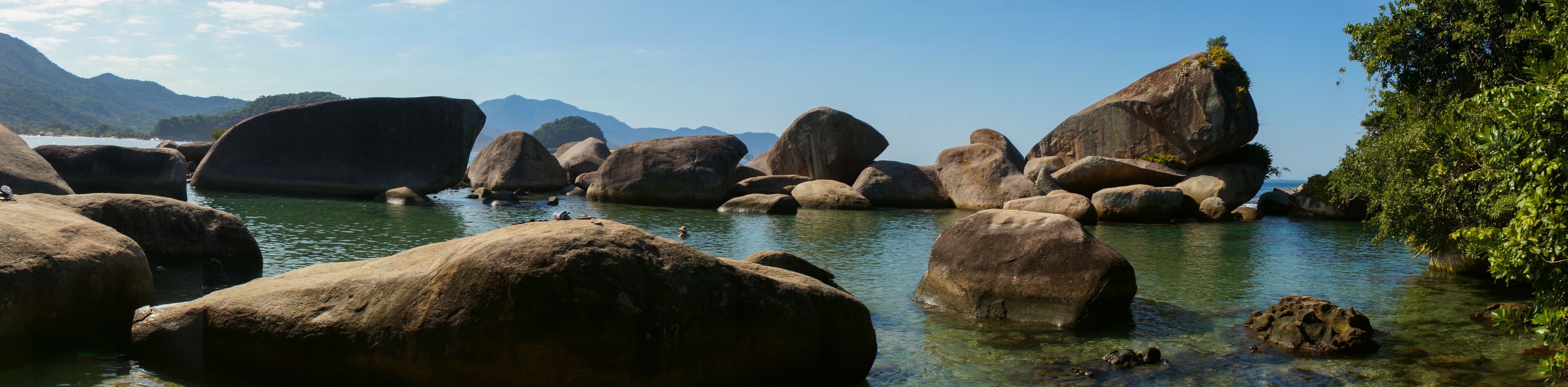 A river with large boulders and clear water surrounded by mountains.