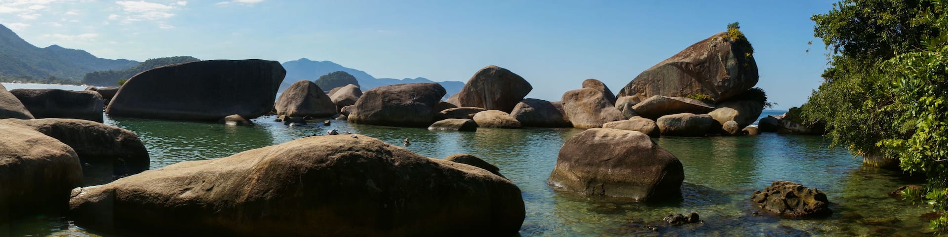 A river with large boulders and clear water surrounded by mountains.