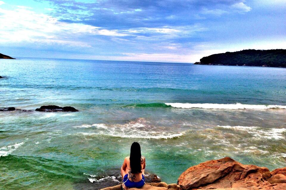 A person sitting on rocks by the sea with waves crashing nearby.
