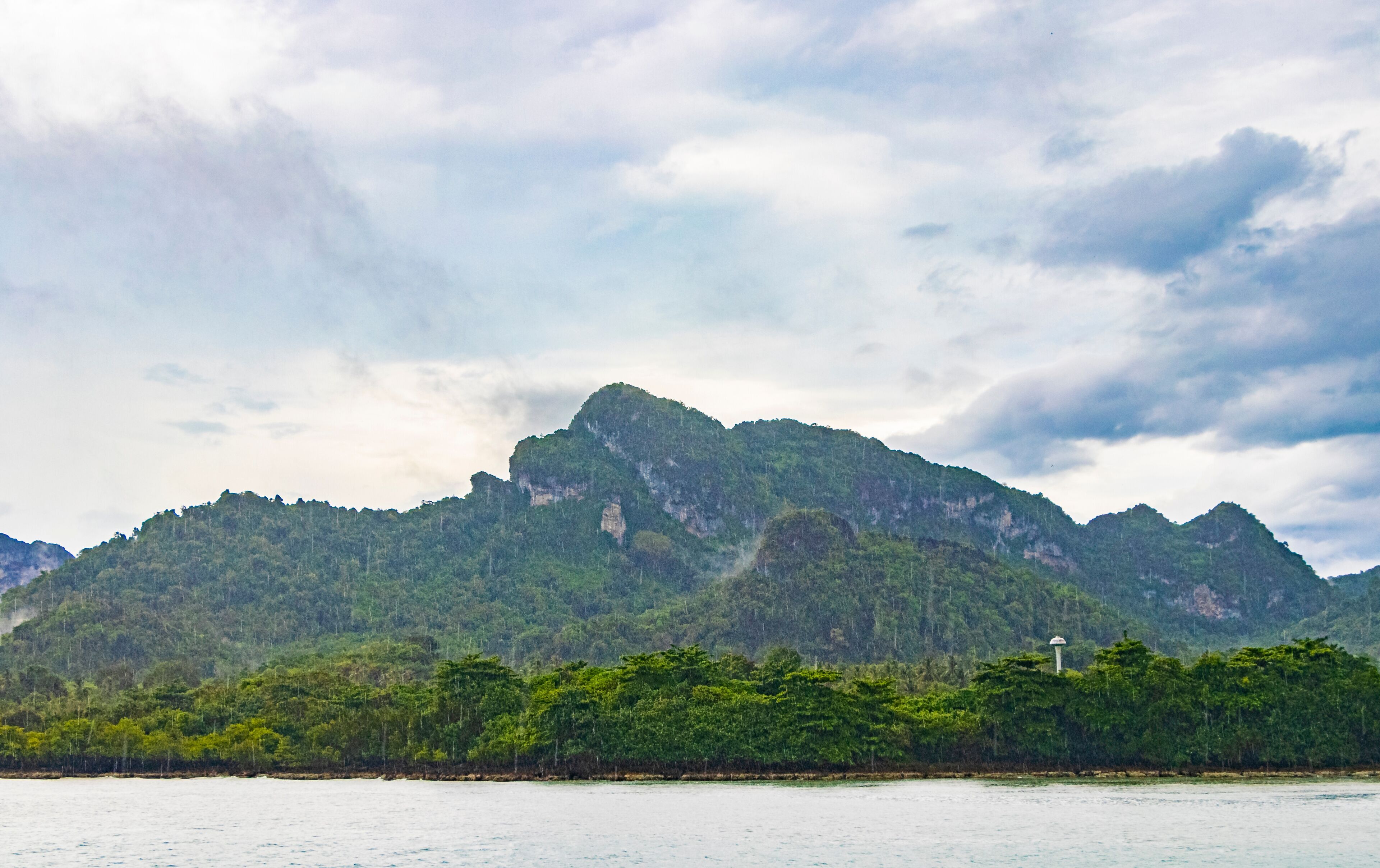 A mountain range with a lighthouse on a coastal forested area.