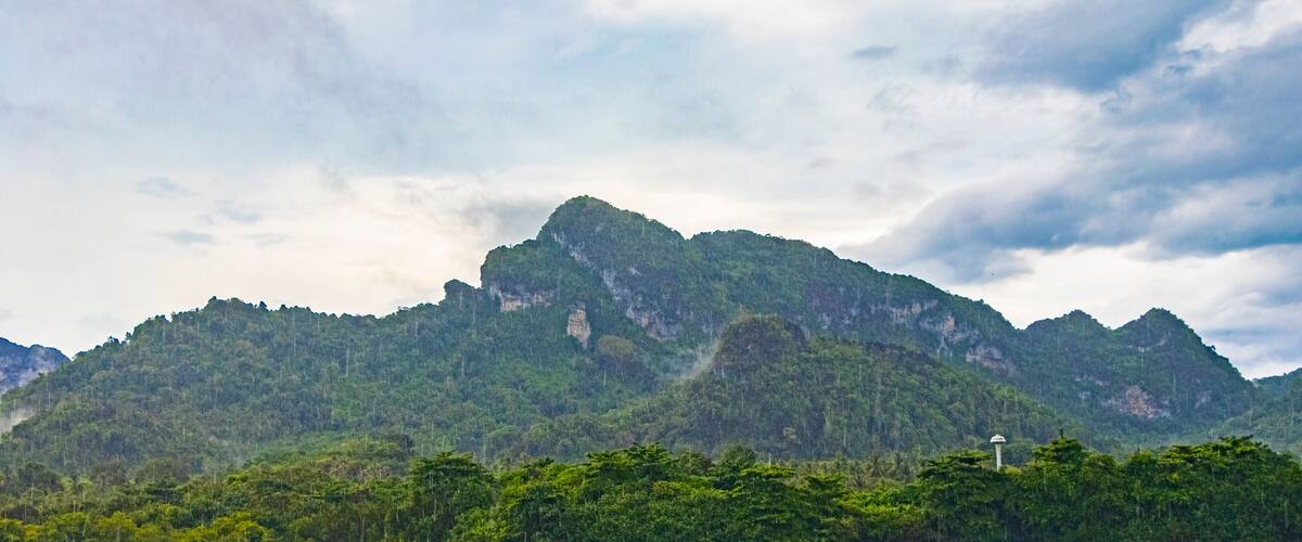 A mountain range with a lighthouse on a coastal forested area.