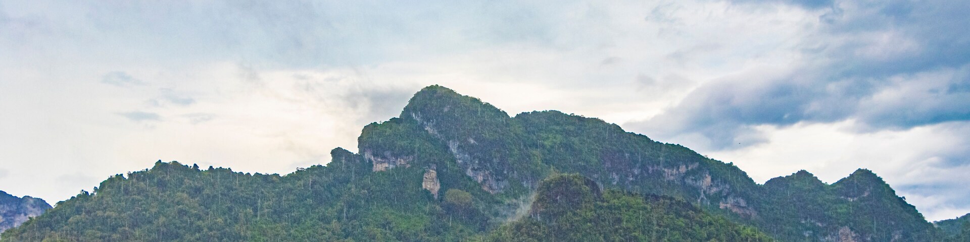 A mountain range with a lighthouse on a coastal forested area.
