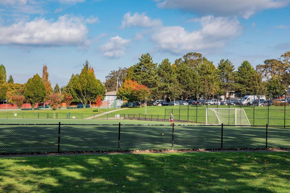 Un camp de futbol amb un pòrtic, envoltat d'arbres i cotxes estacionats.