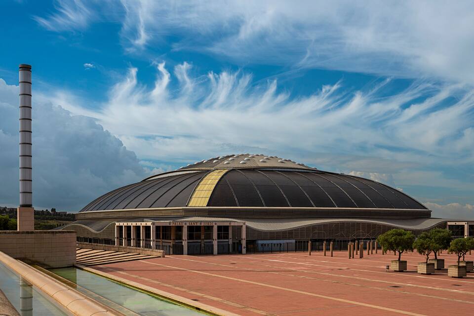 Un grand stade moderne doté d’un toit incurvé et d’une haute cheminée.