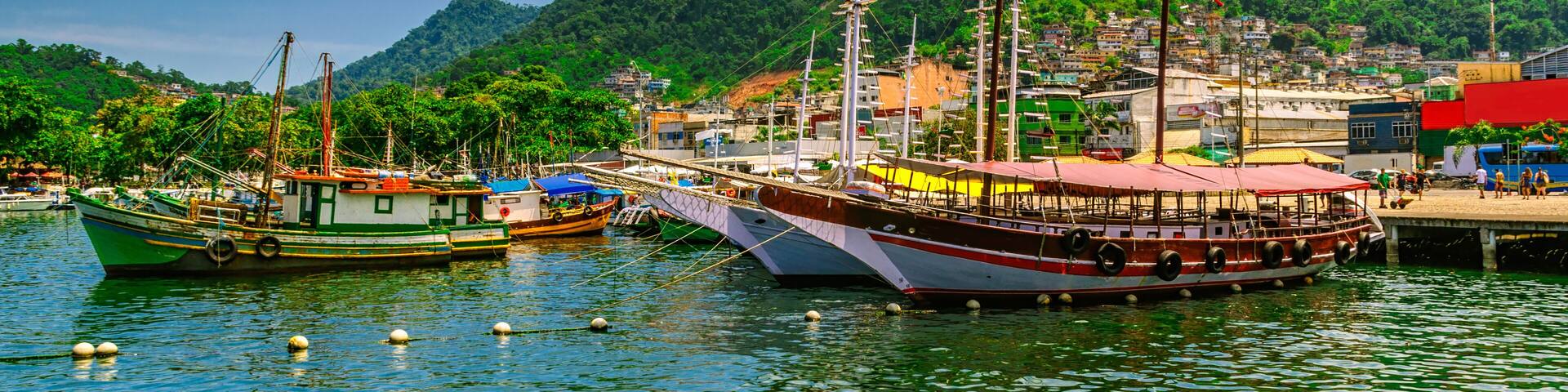 A harbor with boats, a dock, and a green hillside in the background.
