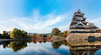 A traditional Japanese castle with a reflection in the water, surrounded by autumn trees and a clear sky.
