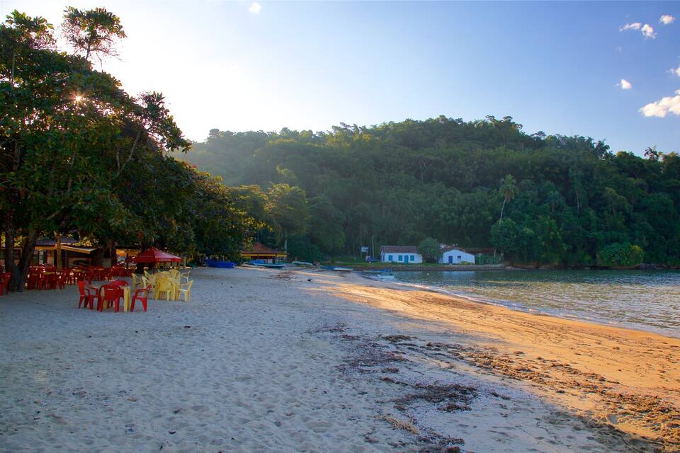 A beach with red and yellow chairs, a small house, and a boat on the water.