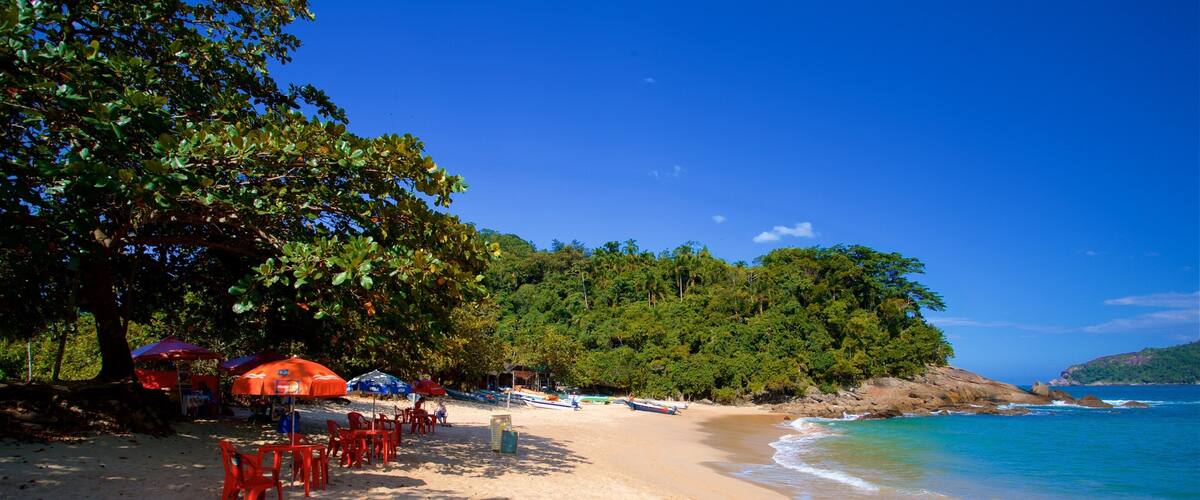 A beach with red umbrellas, a sandy shore, and a forested hill in the background.