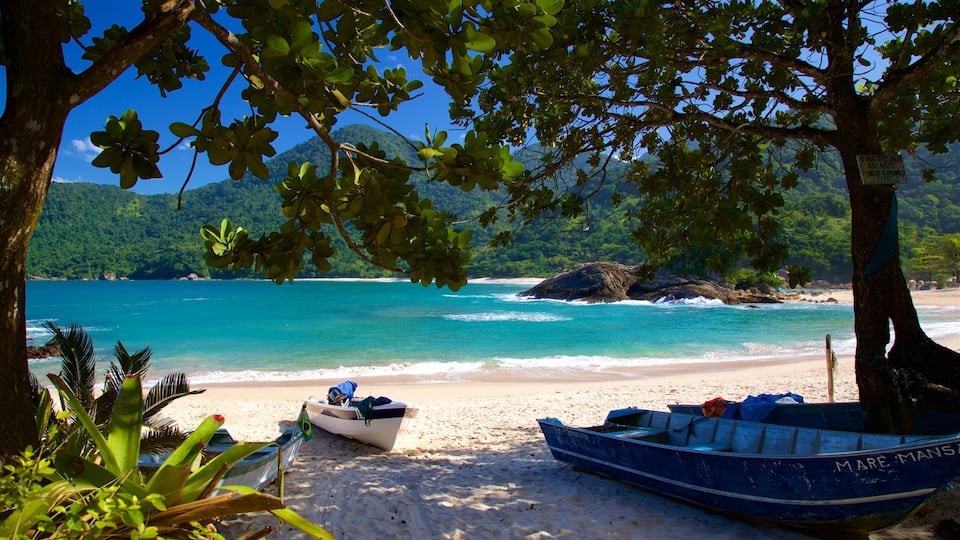 A beach with boats, clear turquoise water, and lush greenery.
