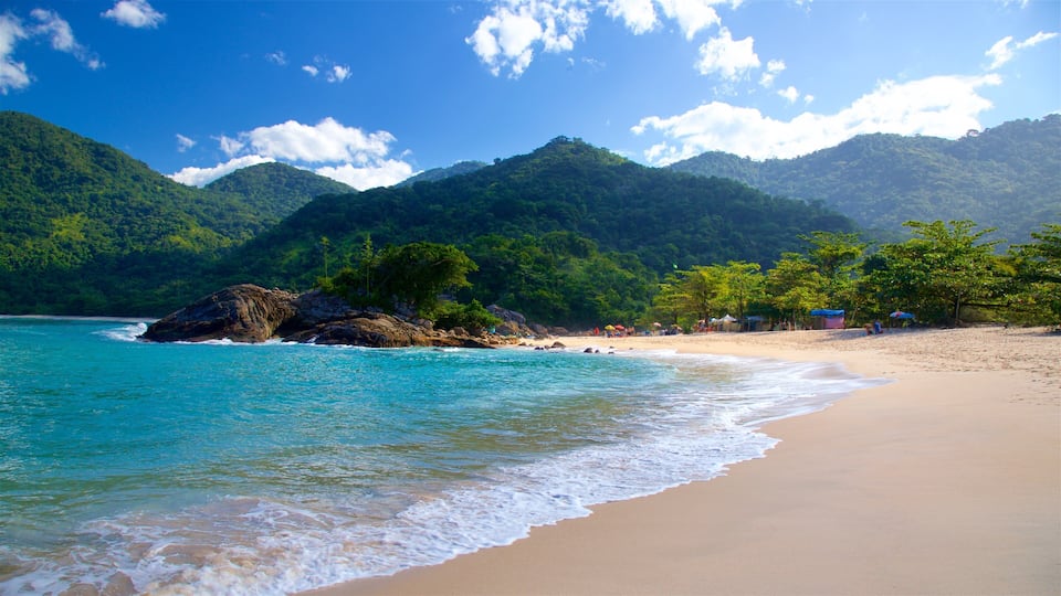 A beach with turquoise water, sandy shore, and green mountains in the background.