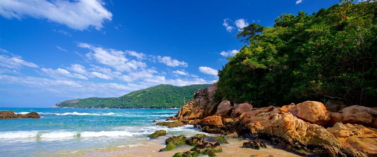 A beach with clear turquoise water, rocky outcrops, and lush green vegetation.