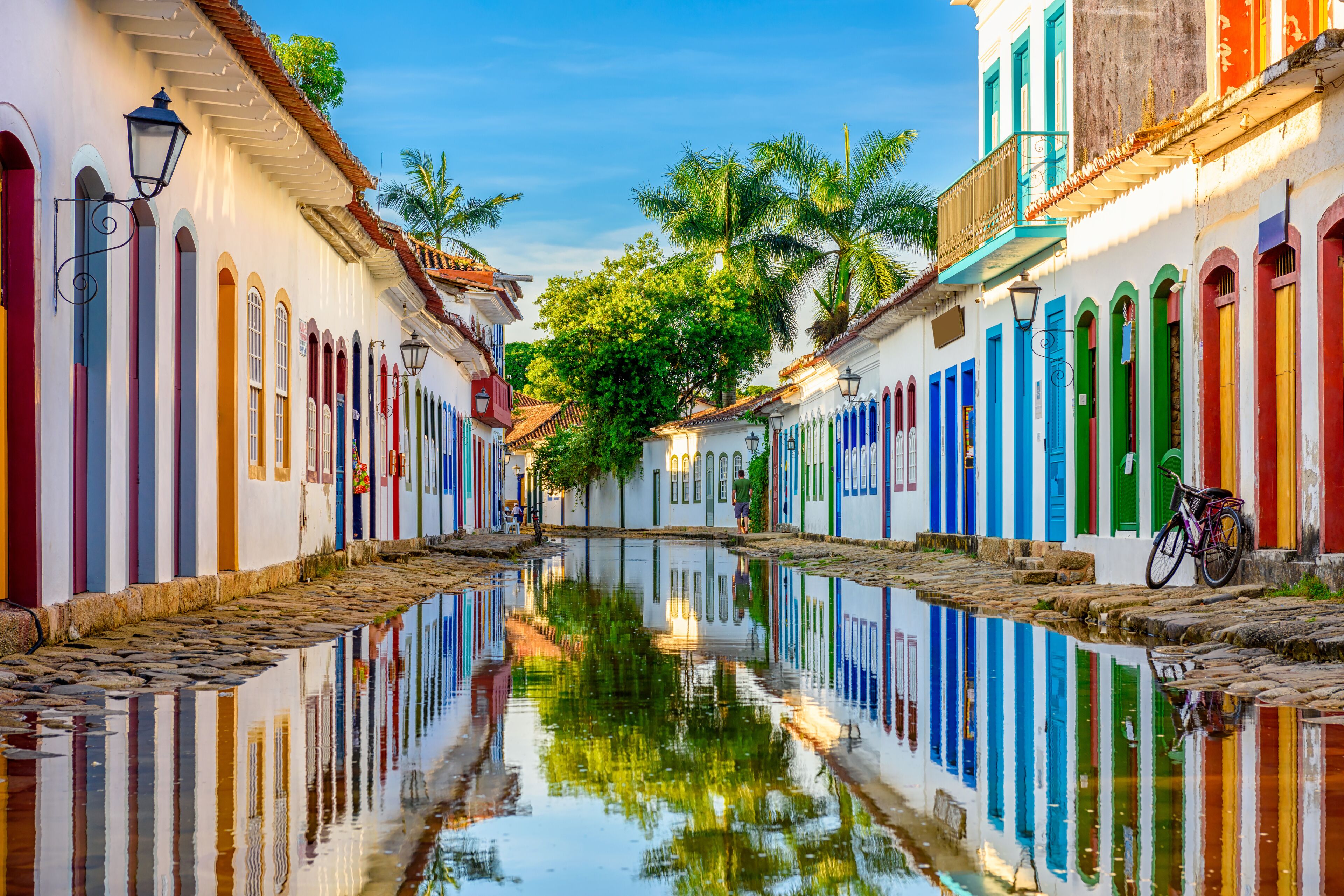 Un canal estrecho bordeado por edificios coloridos con balcones, palmeras y una bicicleta.