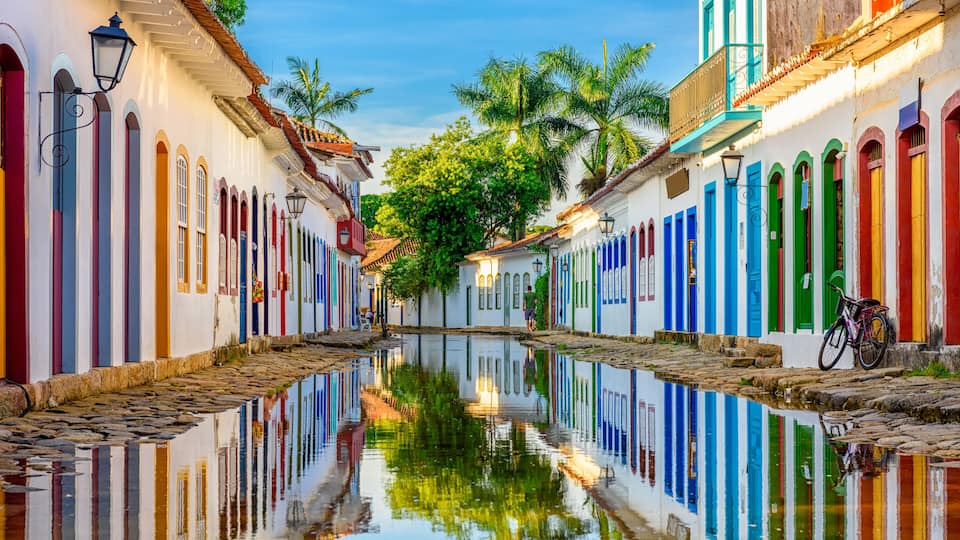 Un canal estrecho bordeado por edificios coloridos con balcones, palmeras y una bicicleta.