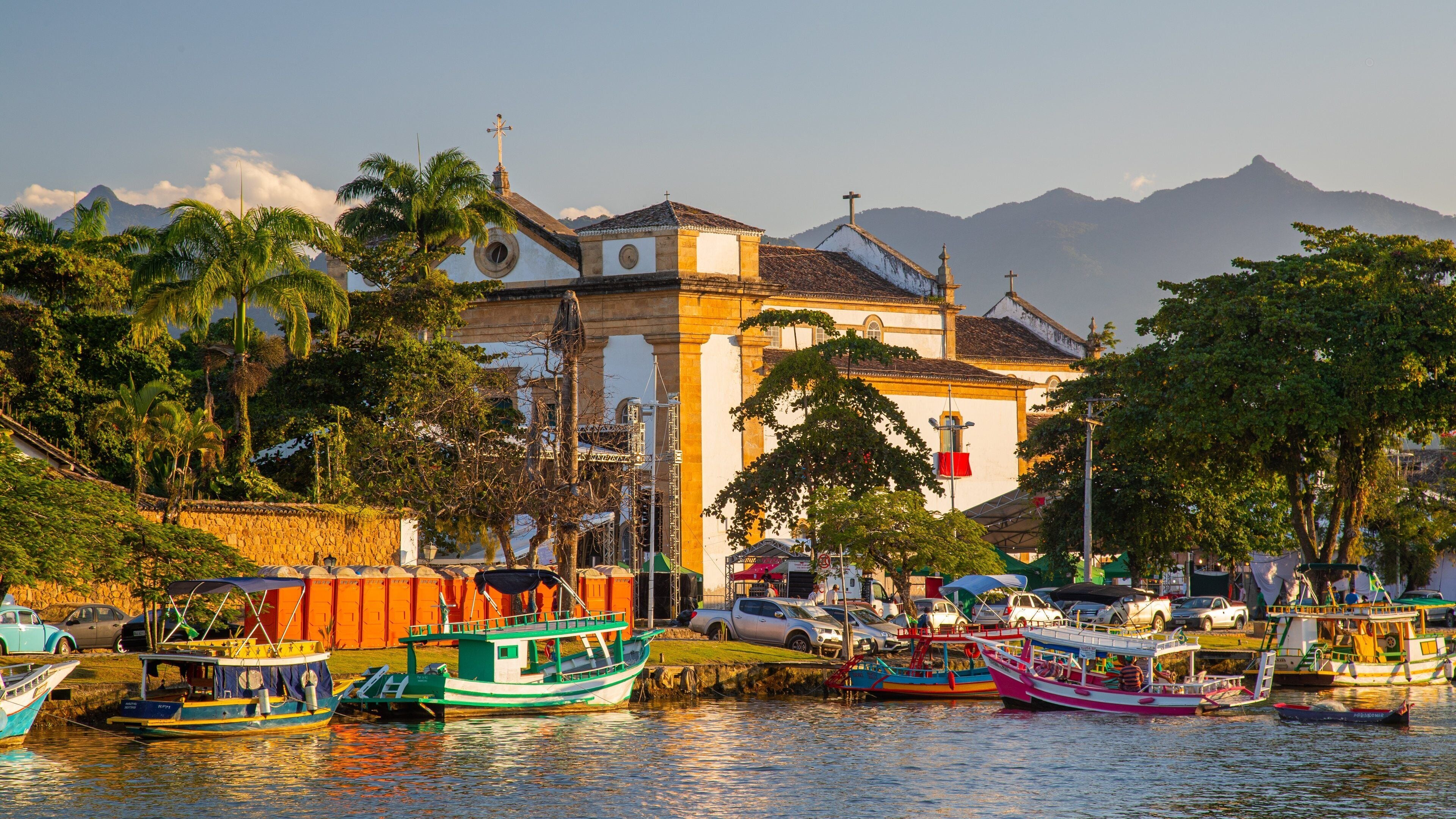 A harbor with colorful boats, a church, and mountains in the background.