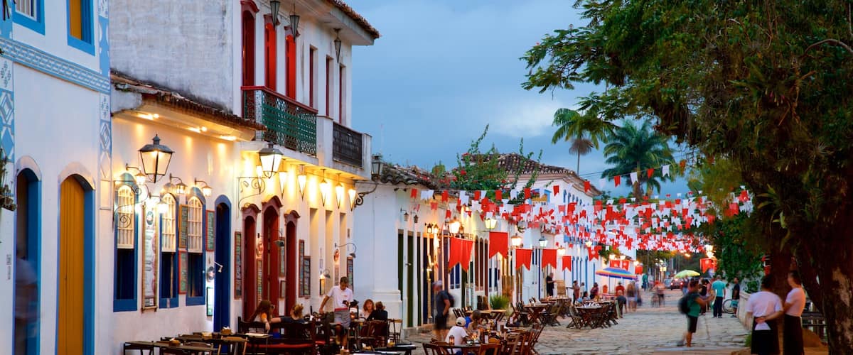 A cobblestone street lined with colorful buildings, outdoor seating, and red and white flags.