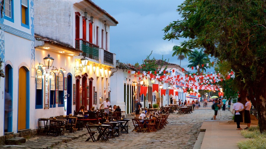 Una calle adoquinada bordeada de edificios coloridos, con mesas al aire libre y banderas rojas y blancas.