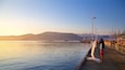 A wooden pier extending into calm waters with boats and a mountainous backdrop during sunset.