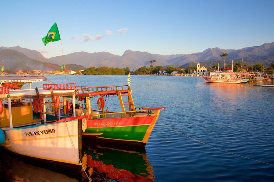 A colorful boat named 'Sol de Verro' docked at a harbor with mountains in the background and a flag flying.
