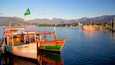 A colorful boat named 'Sol de Verro' docked at a harbor with mountains in the background and a flag flying.