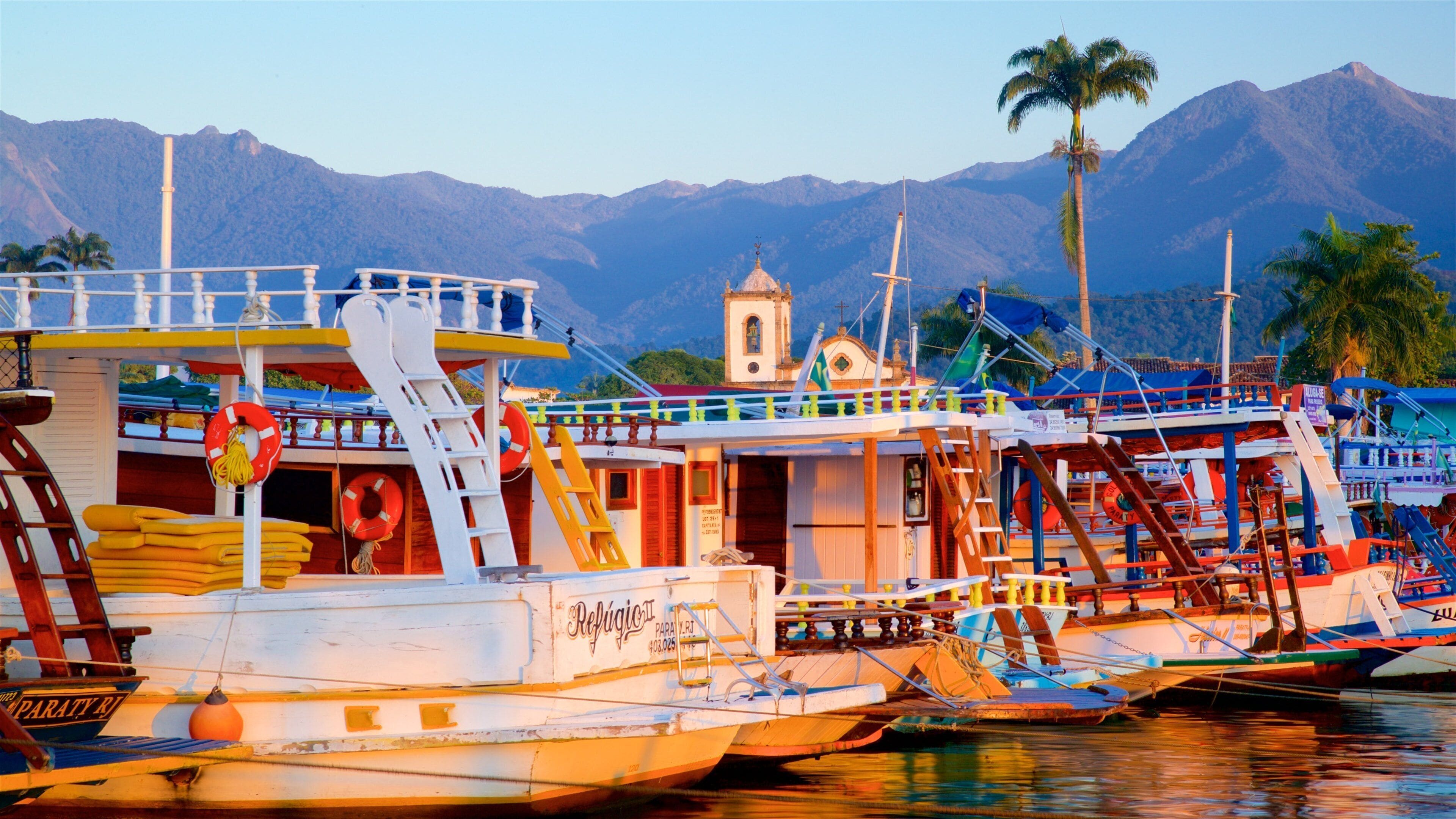 A harbor with boats, a church, and mountains in the background.