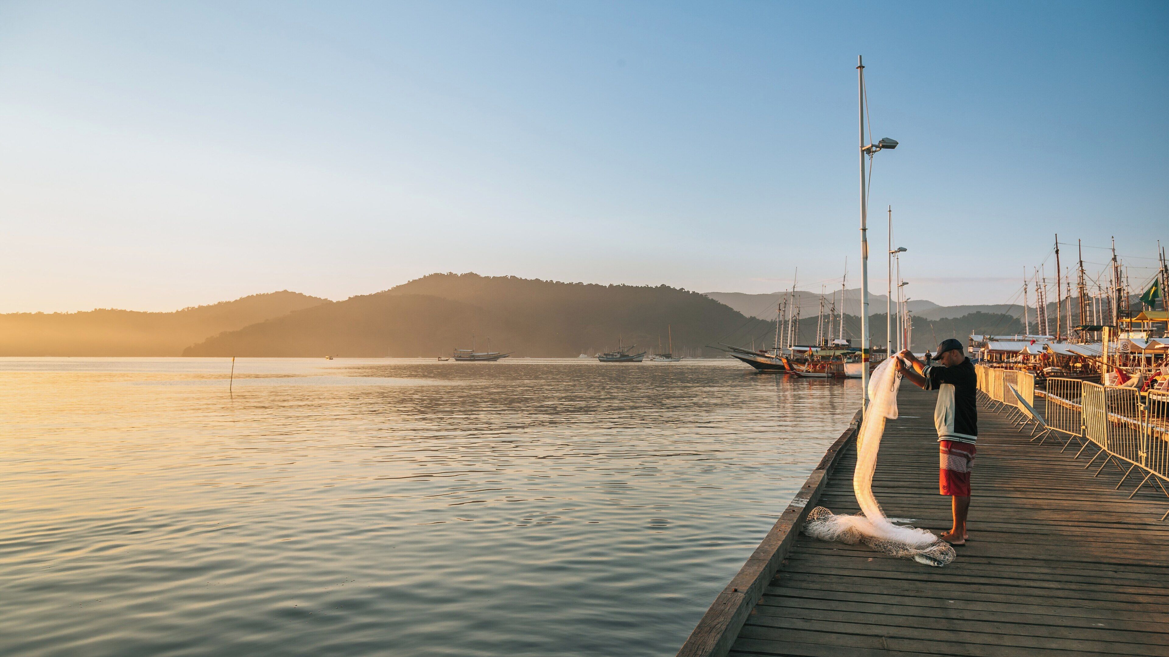 Stunning twilight at Paraty Wharf in Rio de Janeiro with fishermen preparing nets and boats anchored under the warm sunset glow