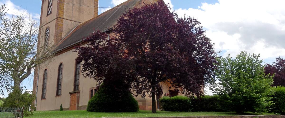 A church with a tall steeple and a clock, surrounded by trees and a brick wall.