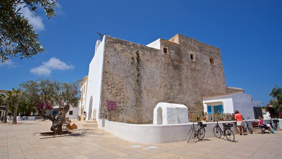 A historic building with a white facade and stone walls, surrounded by a paved square with benches and bicycles.
