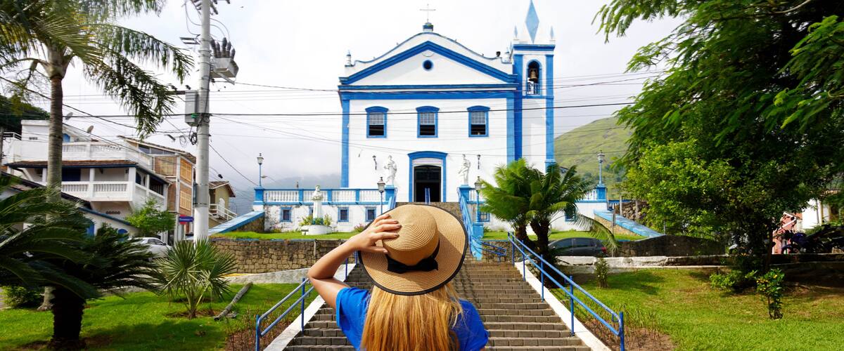 A woman in denim shorts and a blue shirt walking up a brick staircase towards a blue and white church with a bell tower.