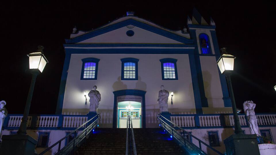 A night view of a building with a blue and white facade, a bell tower, and statues at the entrance.