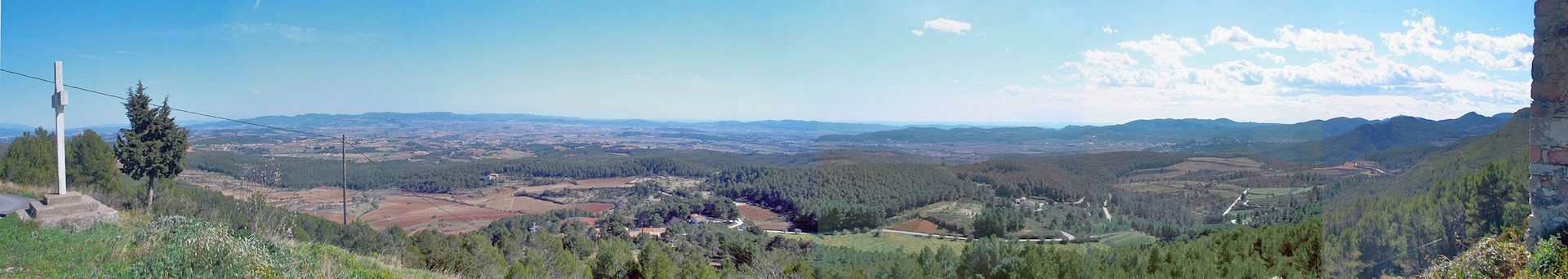 A panoramic view of a valley with a mix of forested areas and agricultural fields, a distant mountain range, and a clear sky.