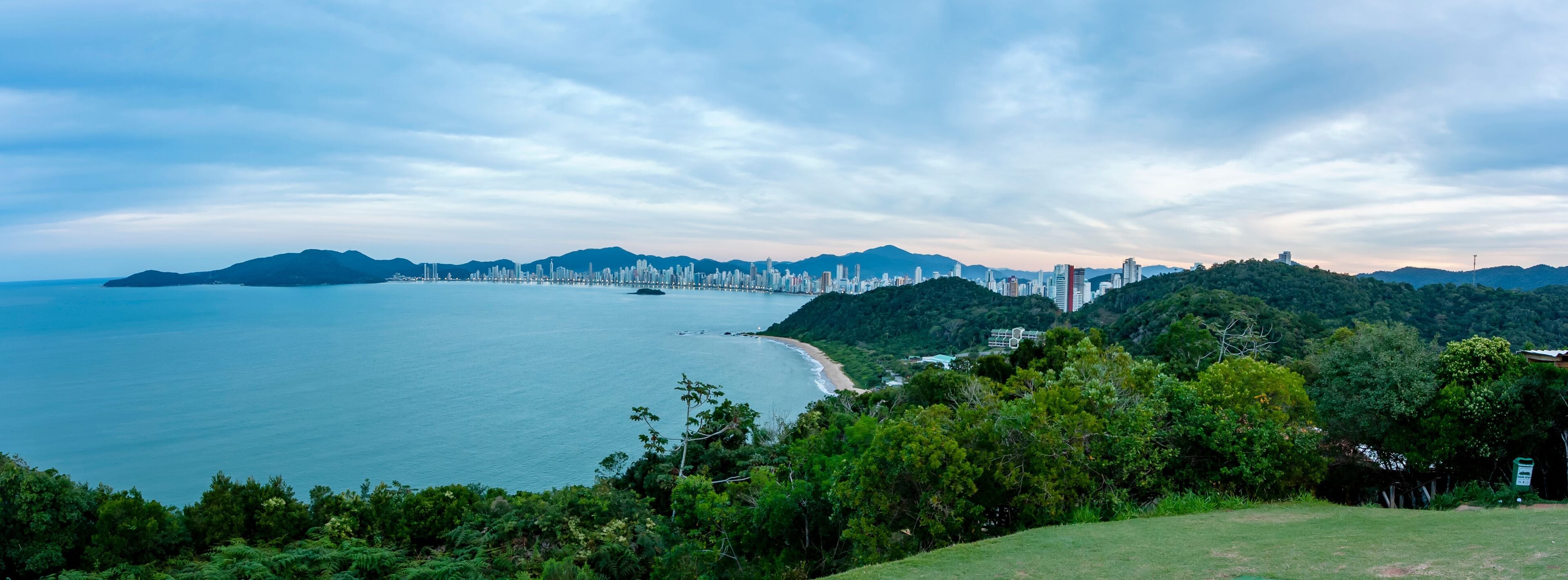 Praia central de Balneário do Camburiú distante durante o anoitecer. Linha de prédios em panorâmica aérea de cima do morro do Careca.