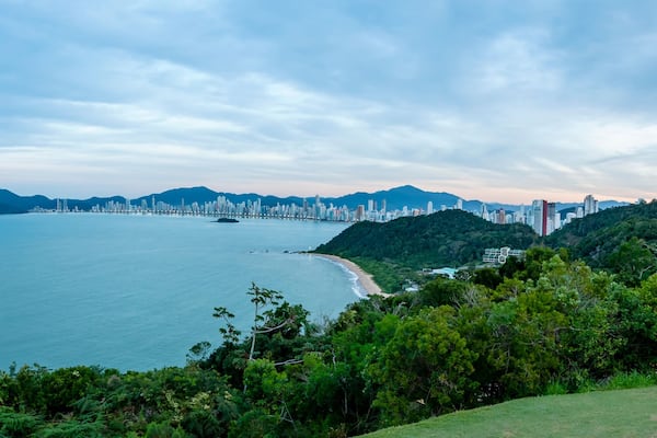 Praia central de Balneário do Camburiú distante durante o anoitecer. Linha de prédios em panorâmica aérea de cima do morro do Careca.