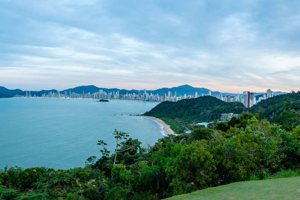 A coastal cityscape with a beach, dense forest, and a mountain range.
