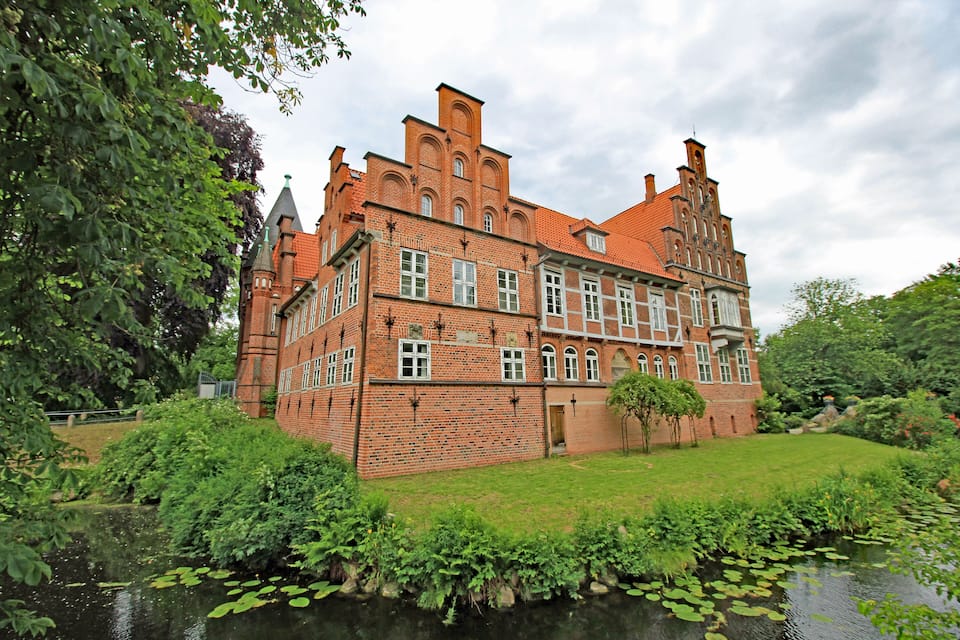 A historic brick building with a large garden and a pond.