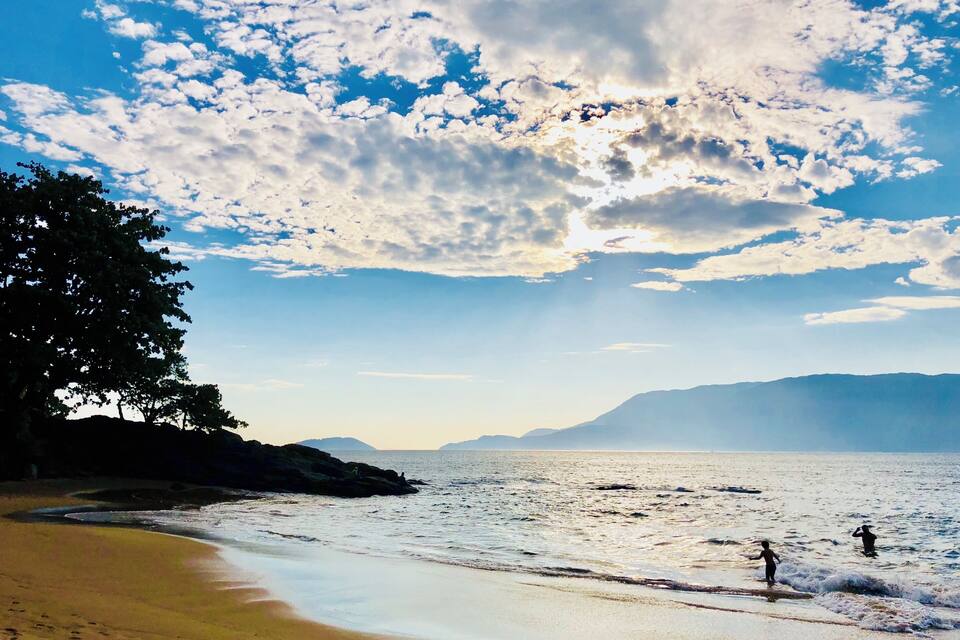 A beach with a clear sky, waves, and distant mountains.