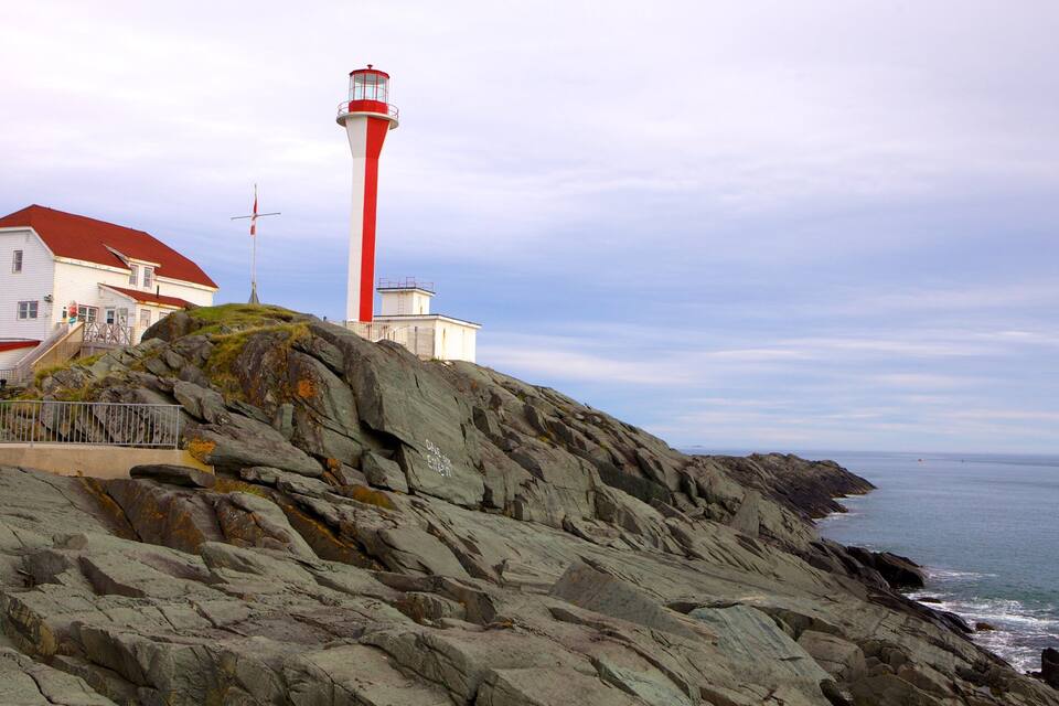 A lighthouse and a white building on a rocky cliff by the sea.
