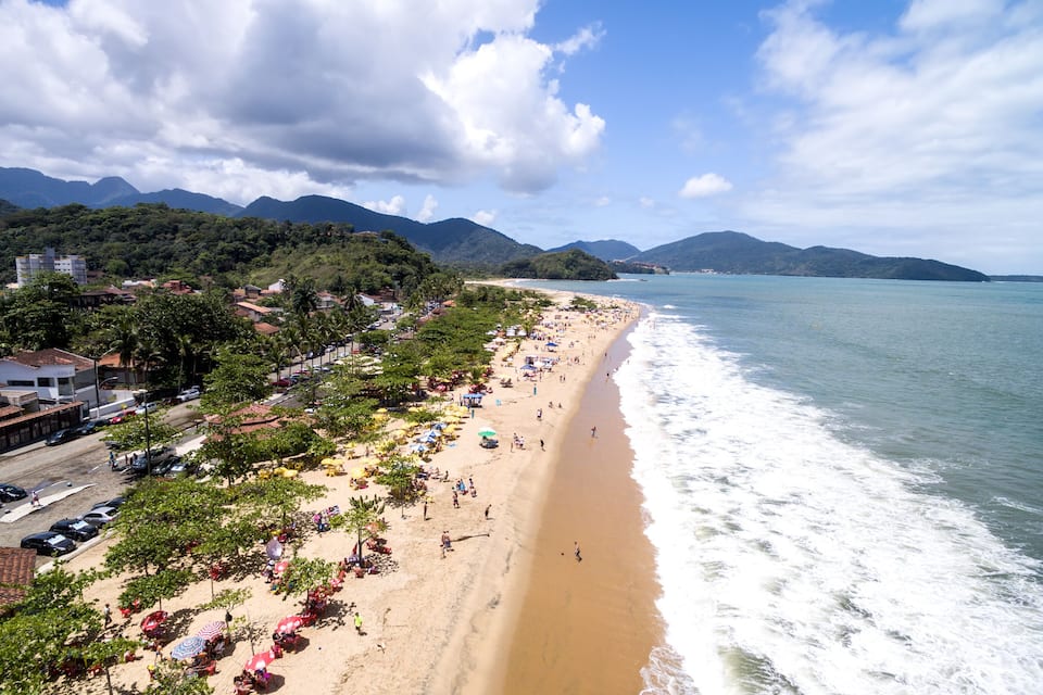 A beach with people, umbrellas, and mountains in the background.