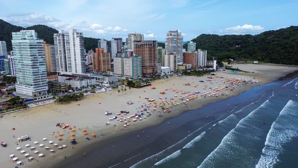 A coastal cityscape with a wide beach, numerous beach umbrellas, and tall buildings.