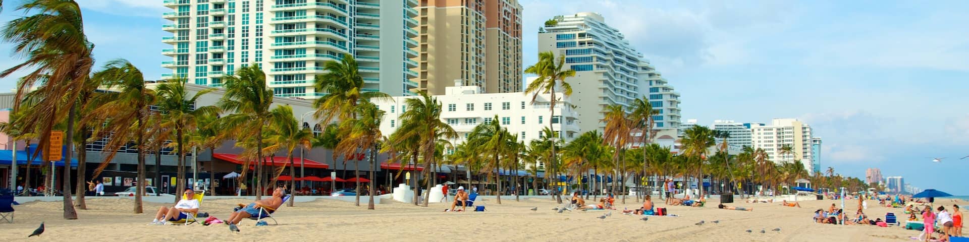 A beach with palm trees and tall buildings in the background.
